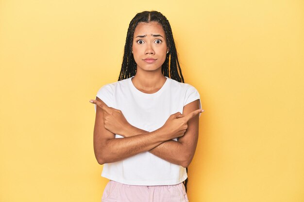 Young Indonesian woman on yellow studio backdrop points sideways