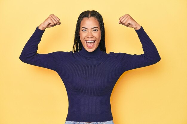 Young Indonesian woman on yellow studio backdrop showing strength gesture with arms