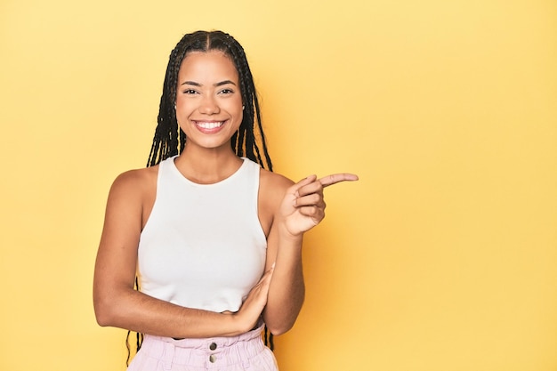 Photo young indonesian woman on yellow studio backdrop smiling cheerfully pointing with forefinger away