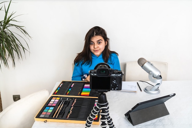 Young influencer and blogger livestreaming a crayon painting class from her living room laughing and looking into the camera and speaking into the microphone on a video or social media platform