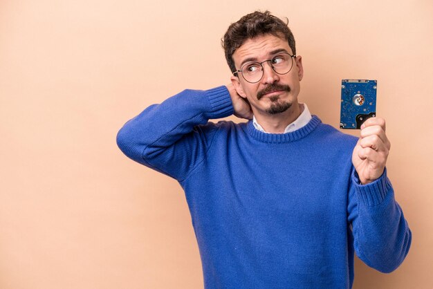 Young informatic man isolated on beige background touching back of head, thinking and making a choice.