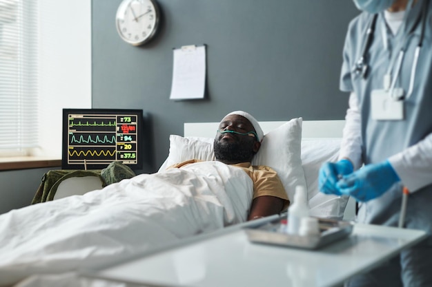Молодой раненый мужчина с перевязанной головой лежит в постели в больничной палате