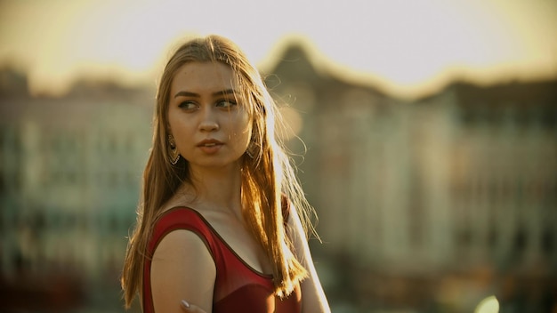 A young inspired woman with big earrings standing on the roof bright sunset