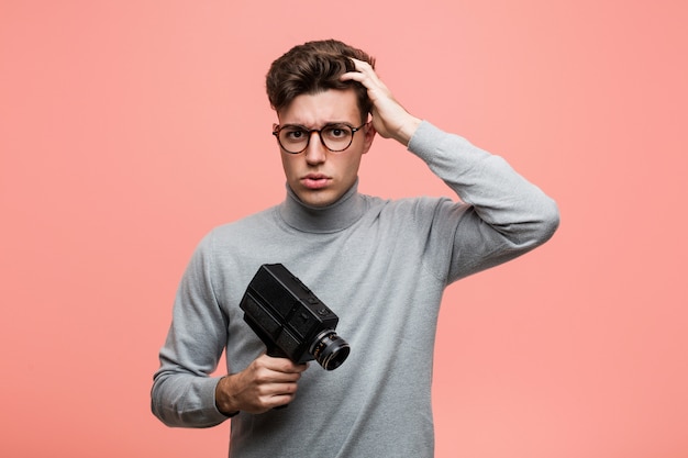 Young intellectual man holding a film camera being shocked, she has remembered important meeting.