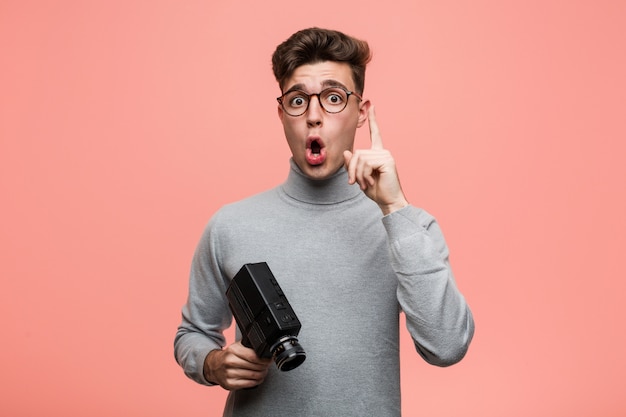 Young intellectual man holding a film camera having some great idea, concept of creativity.