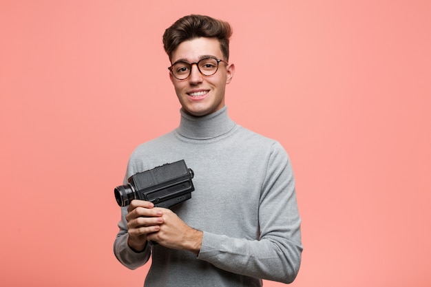 Young intellectual man holding a film  happy, smiling and cheerful.