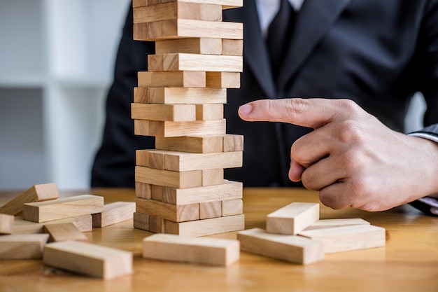 Young intelligent businessman playing the wood game, hands of executive placing wood block