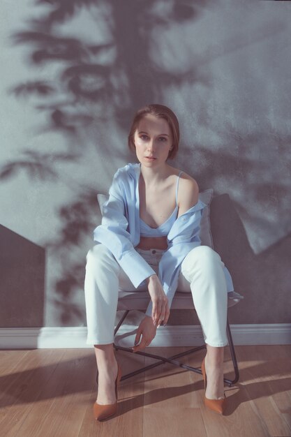 Young intelligent well-dressed in white-blue stylish Caucasian woman sitting on a chair