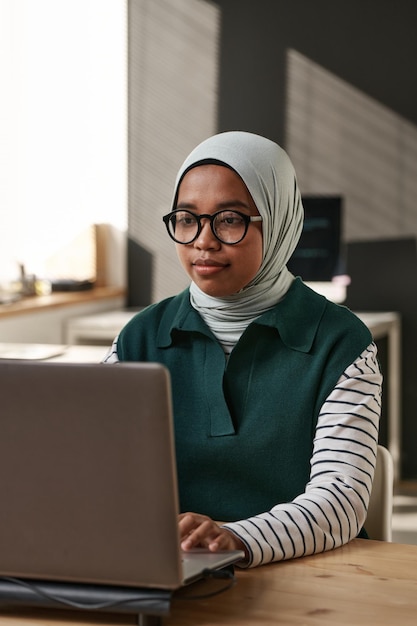 Hijab와 노트북 앞에 앉아 다 디코딩 안경에 젊은 이문화 사업가