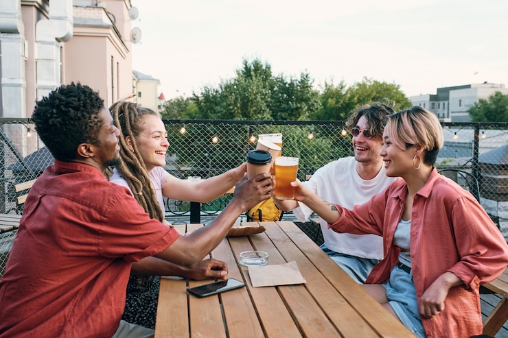 Photo young intercultural friends toasting with drinks over wooden table