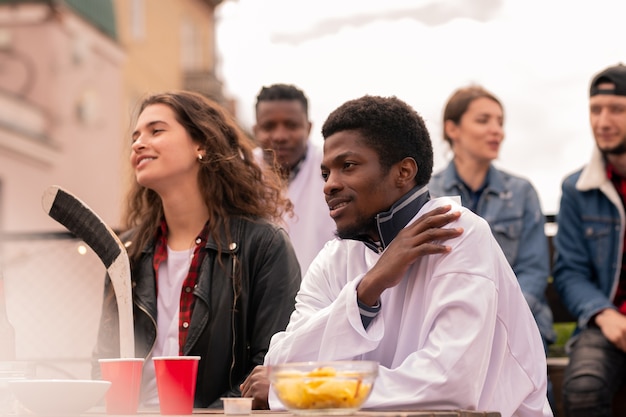 Young intercultural hockey fans watching match broadcast while having drinks and snack in urban environment