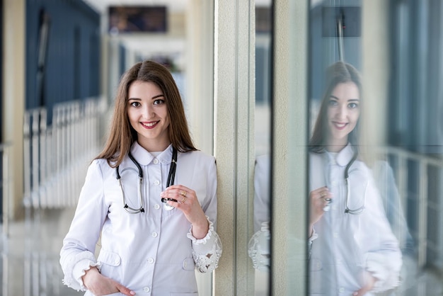 A young intern in a gown with a stethoscope poses for the camera in the hospital