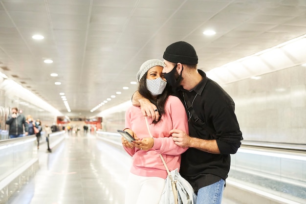 A young interracial couple of lovers wearing masks and wool hats in a subway corridor