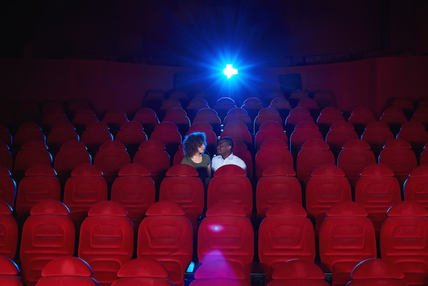 Young interracial couple sitting in an empty cinema hall watching a movie together copyspace love romance vip romantic anniversary date entertainment activity concept.