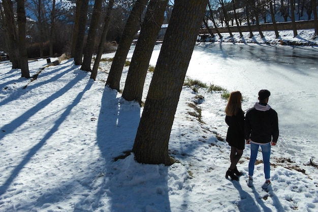 雪の背景に氷の川を見ている若い異人種間のカップル。旅行と休暇のコンセプト。バレンタインデーのお祝い