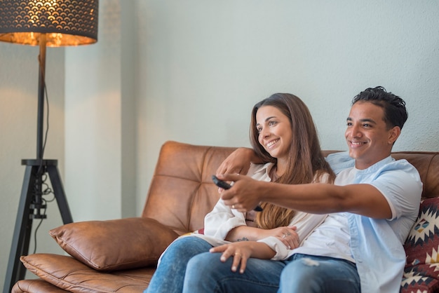 Young interracial couple watching tv together sitting on the sofa at home  couple life and happy lifestyle people having with movie  indoor leisure activity black boy and caucasian girl in love