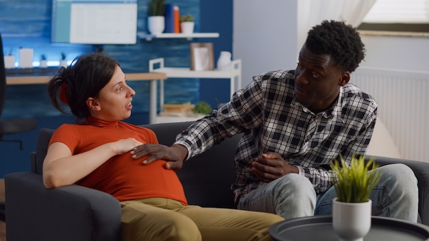 Young interracial couple with pregnancy chatting about baby