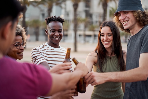 Young interracial people toasting with beer outside