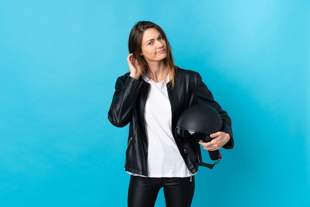 Young ireland woman holding a motorcycle helmet isolated on blue background having doubts