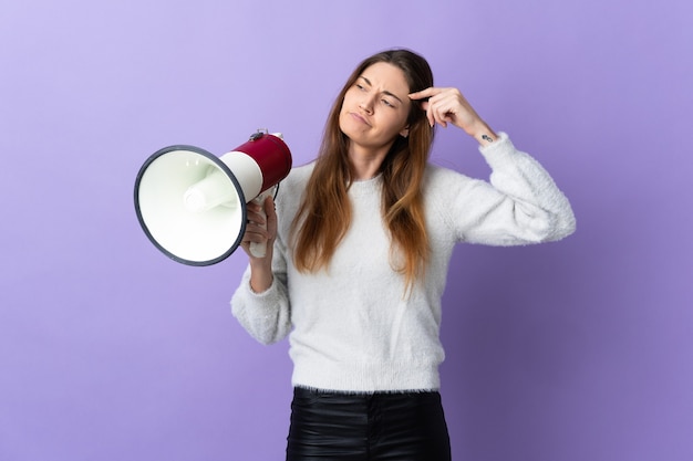 Young Ireland woman isolated on purple background holding a megaphone and having doubts