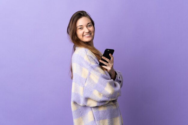 Young ireland woman isolated on purple background holding a mobile phone and with arms crossed