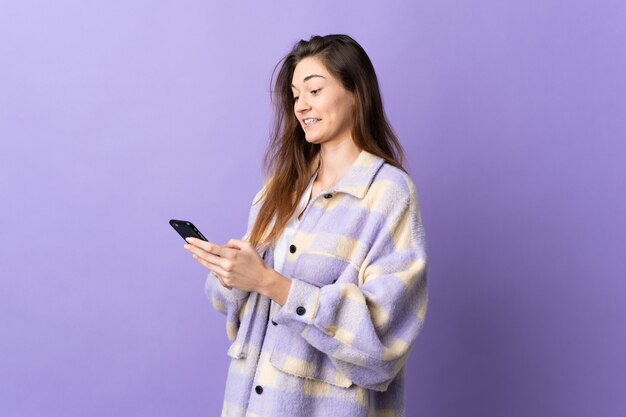 Young Ireland woman isolated on purple background sending a message or email with the mobile