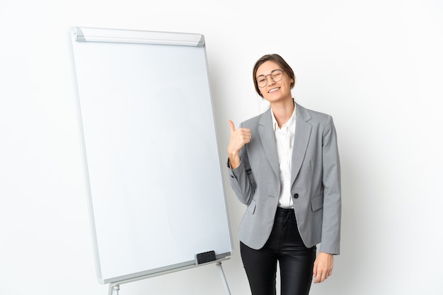 Young Ireland woman isolated on white wall giving a presentation on white board and with thumbs up