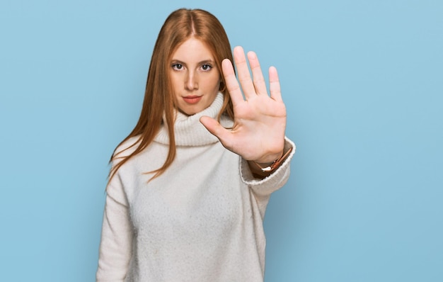 young irish woman wearing casual winter sweater doing stop sing with palm of the hand. warning expression with negative and serious gesture on the face.