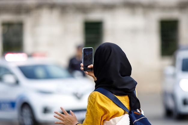 Young islamic woman taking photos on phone back view shooting\
video with cell phone camera using smartphone to take pictures\
outdoor tourist photographing landscape