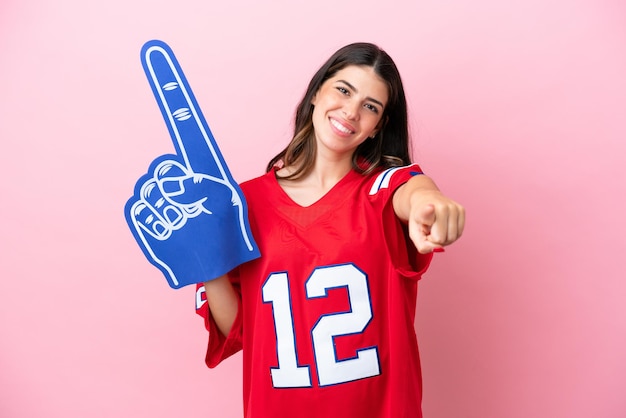 Young Italian fan woman with foam hand isolated on pink background pointing front with happy expression