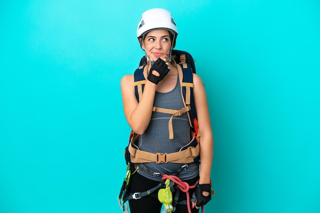 Young Italian rockclimber woman isolated on blue background having doubts and with confuse face expression