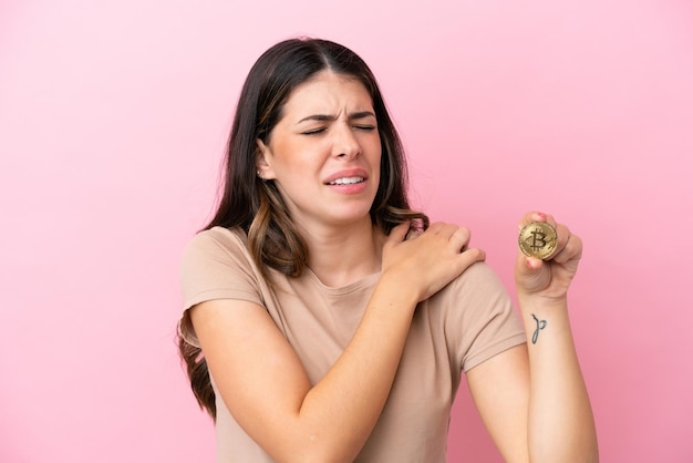 Young Italian woman holding a Bitcoin isolated on pink background suffering from pain in shoulder for having made an effort