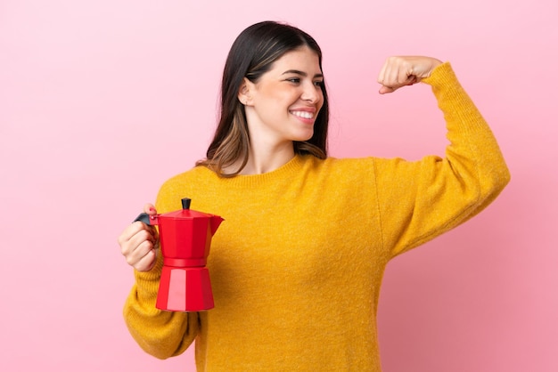 Young Italian woman holding a coffee maker isolated on pink background doing strong gesture