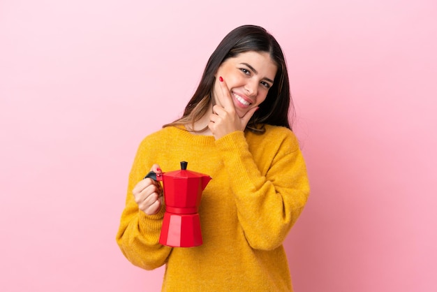 Young Italian woman holding a coffee maker isolated on pink background happy and smiling