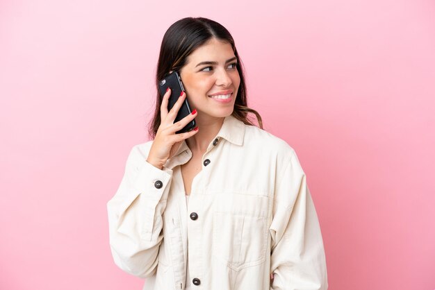 誰かと携帯電話との会話を維持しているピンクの背景に分離された若いイタリア人女性