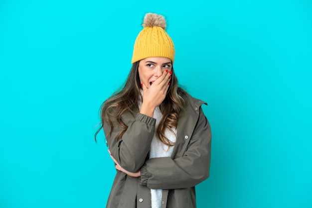 Young Italian woman wearing winter jacket and hat isolated on blue background surprised and shocked while looking right