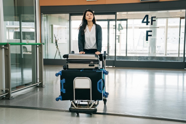 彼女の国を離れて留学に行く日本の若い女の子。多くの荷物を持って一人で空港を歩いているかわいい学生。飛行機カウンターの看板を見つけたエレガントな女性。