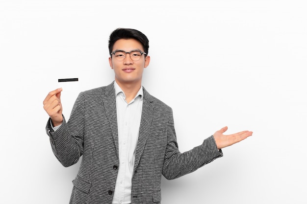 Young japanese man smiling cheerfully, feeling happy and showing a concept in copy space with palm of hand. credit card concept.