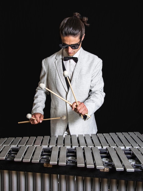 Young jazz musician playing the vibraphone in his private rehearsal room Dressed in white suit white shirt and bow tie Sun glasses