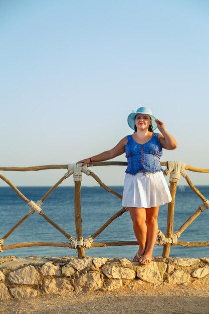 Young Jewish woman in a white skirt and blue hat on the seashore happy. Vertical photo