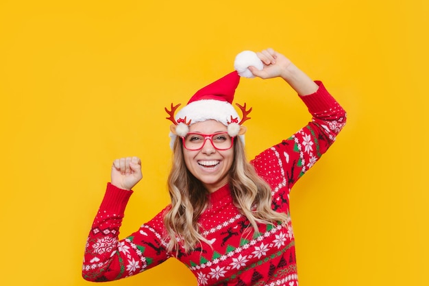 A young joyful blonde girl in a Christmas red deer sweater funny glasses is happy with her hands up