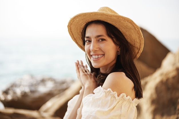 Young joyful brunette woman posing against sea and rocks