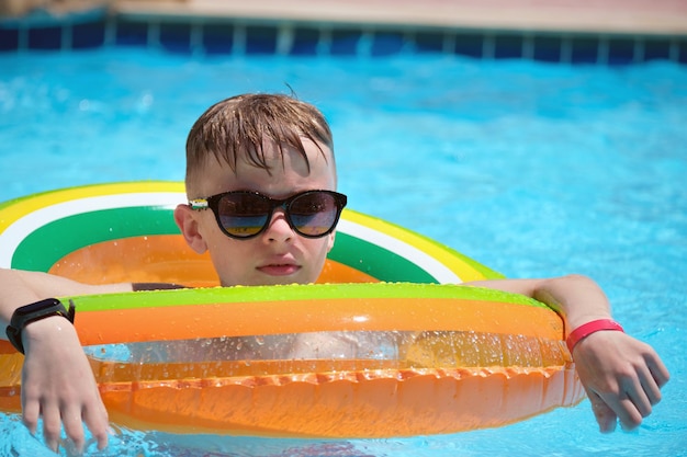 열대 휴가 여름 활동 개념의 따뜻한 여름날 푸른 물이 있는 수영장에서 풍선 공기 원에서 즐겁게 수영하는 어린 소년