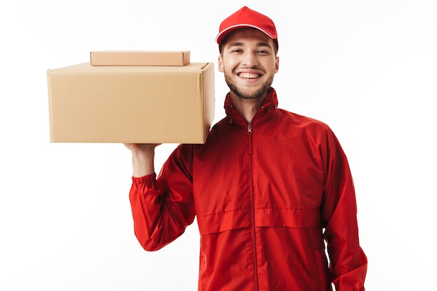 Young joyful delivery man in red cap and jacket holding parcel in hand happily 