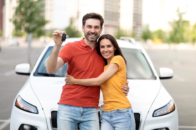 屋外の新しい車の近くに立っている若い楽しい男性と女性