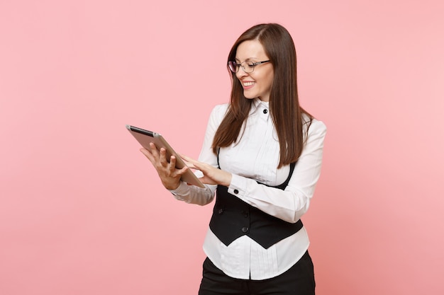 Young joyful successful attractive business woman holding and using tablet pc computer isolated on pastel pink background. Lady boss. Achievement career wealth concept. Copy space for advertisement.