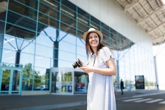 Молодой радостный путешественник турист женщина, держащая ретро винтаж фотоаппарат, глядя в сторону в международном аэропорту