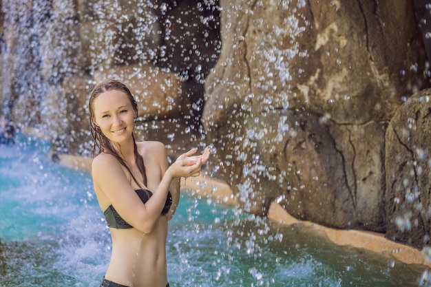 Foto giovane donna gioiosa sotto le sorgenti calde della stazione termale di giorno della piscina del flusso dell'acqua