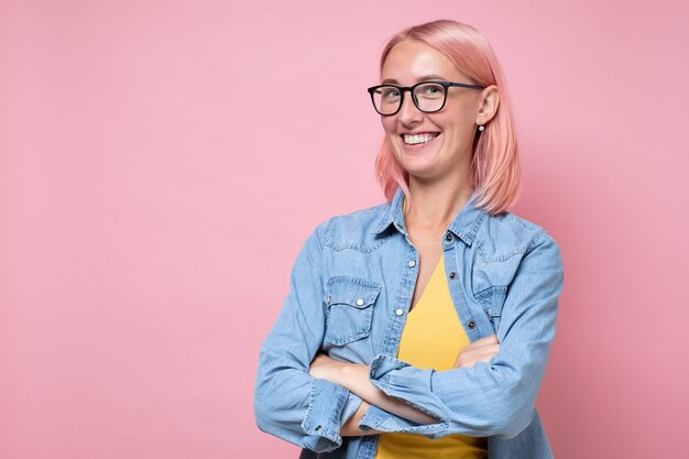 Young joyful woman with pink dyed hair and glasses smiling at camera.