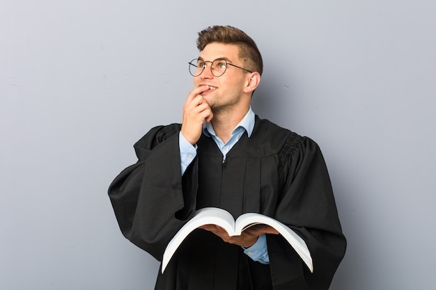 Young jurist holding a book relaxed thinking about something looking at a copy space.